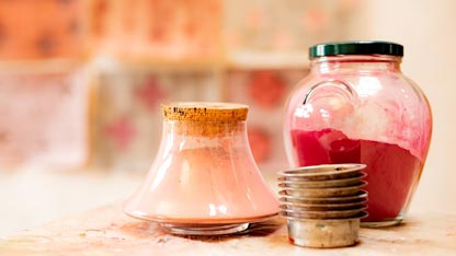 Clear glass jar containing red pigment and tools for mixing