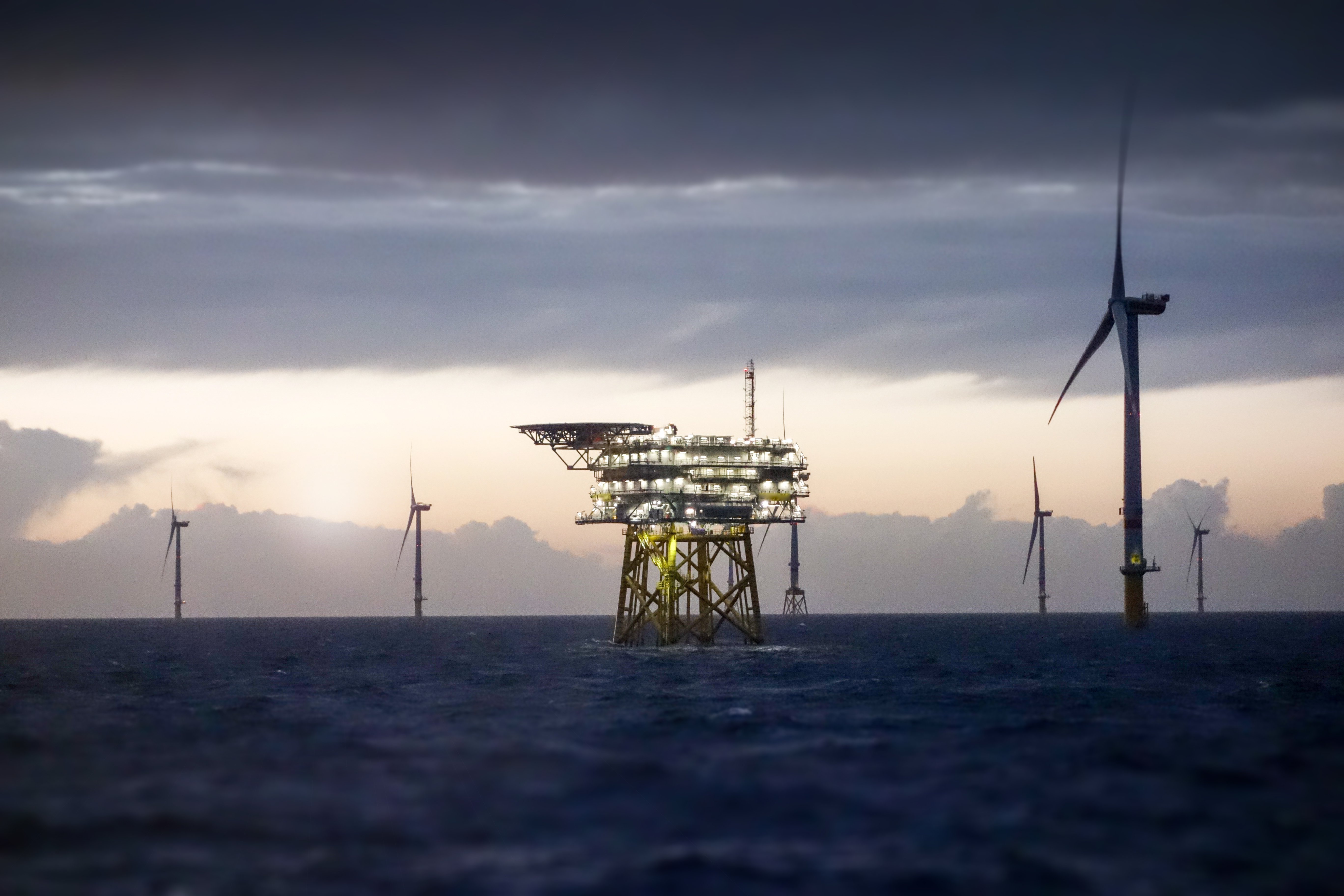 dark skies over a large body of water with an offshore wind farm and offshore electrical transmission platform in view