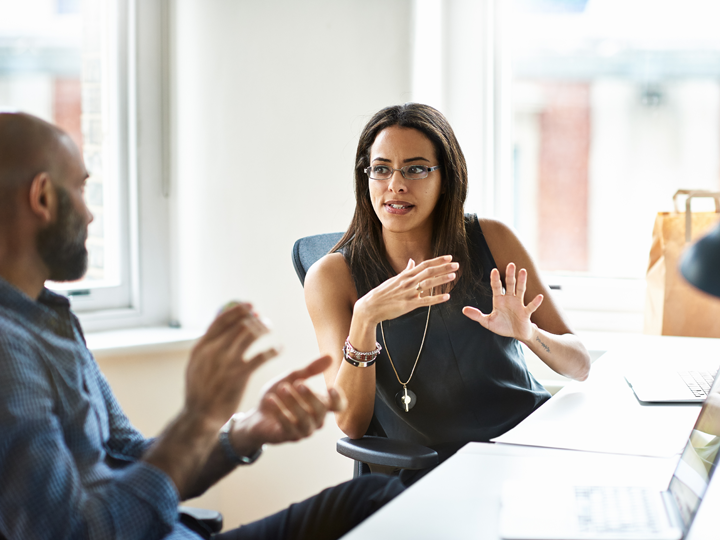 Two colleagues sitting at an office desk discussing