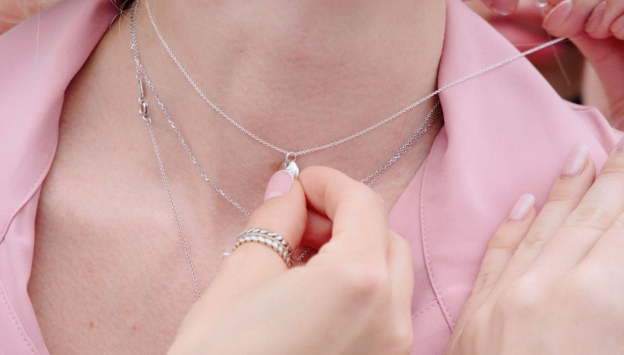 woman in a pick shirt holding a pendant attached to a silver chain necklace