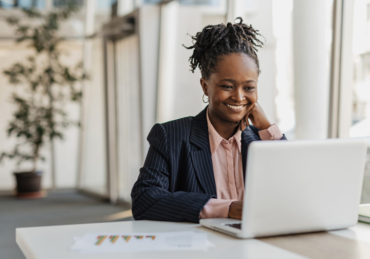 A woman smiles sitting in front of a laptop. 