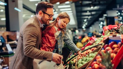 A man and a young girl examine a variety of colorful fruits and vegetables together in a market setting.