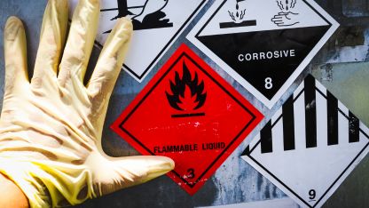 A gloved hand holds a sign warning about hazardous chemicals, emphasizing safety and caution in handling dangerous substances.