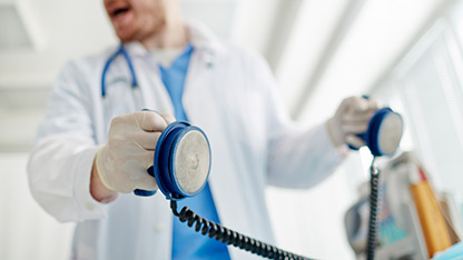 Doctor holding defibrillator paddles, preparing to deliver a shock in a medical emergency setting.