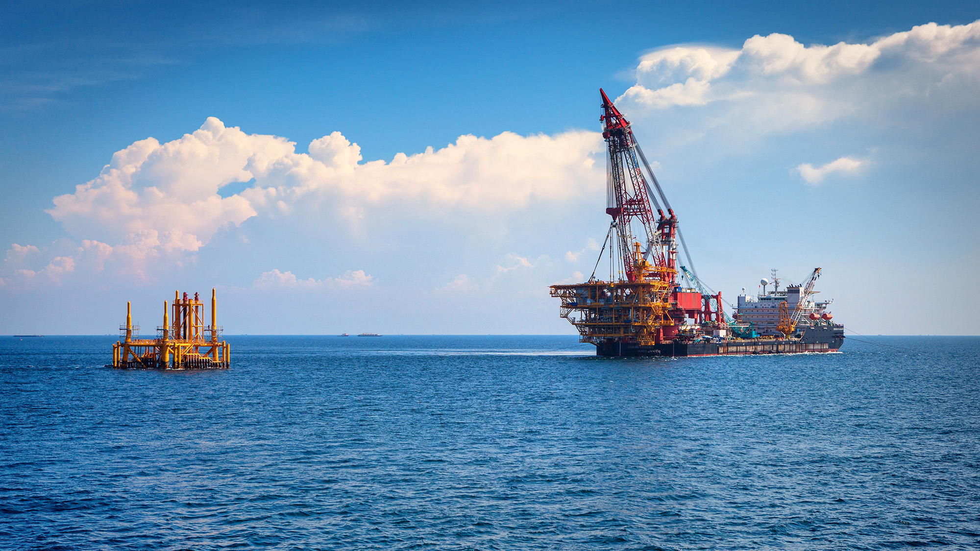offshore oil rig being dismantled and a portion of it is being moved away on a shipping vessel 